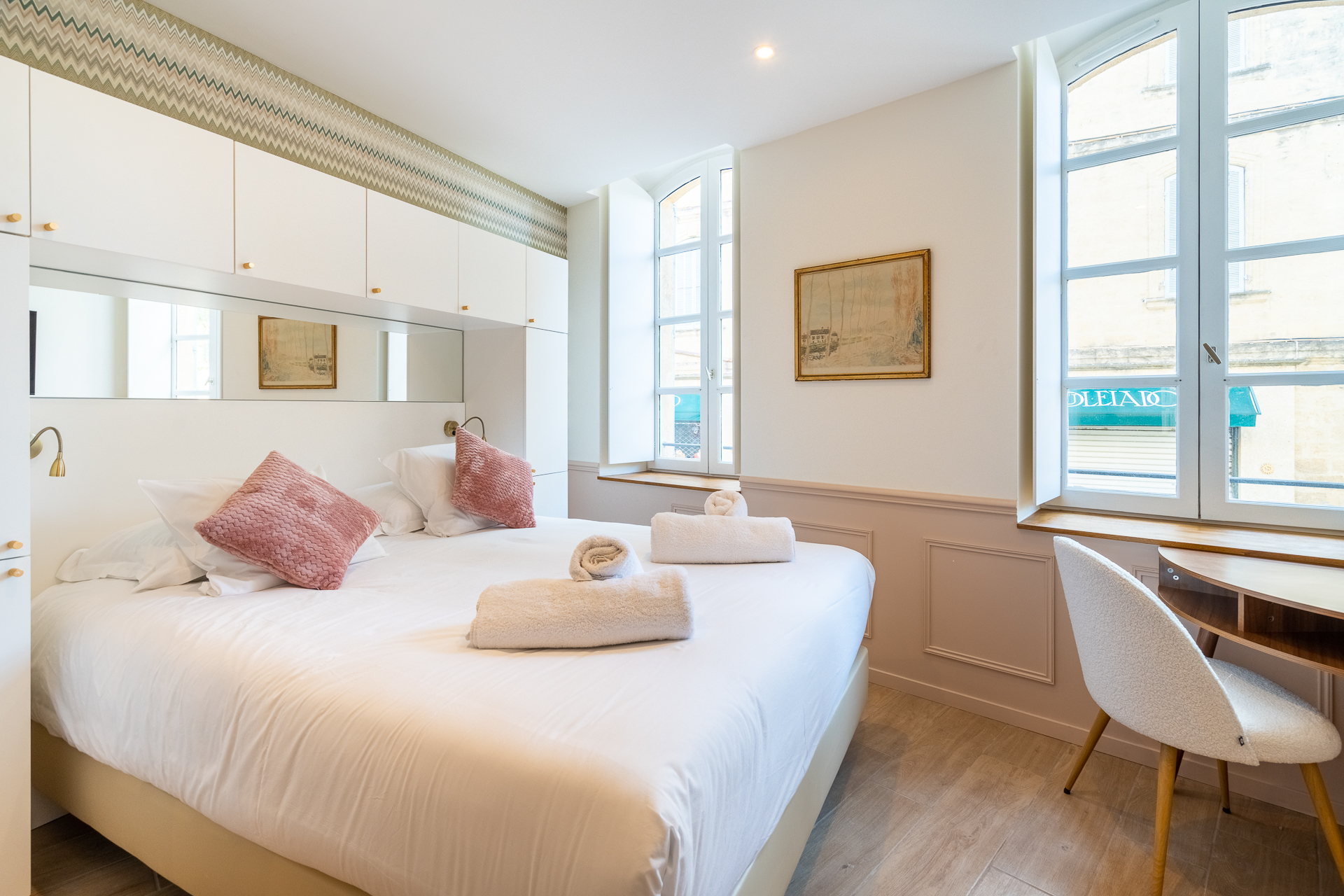 Chambre Deluxe : lit aux coussins rose poudré et fenêtres cintrées