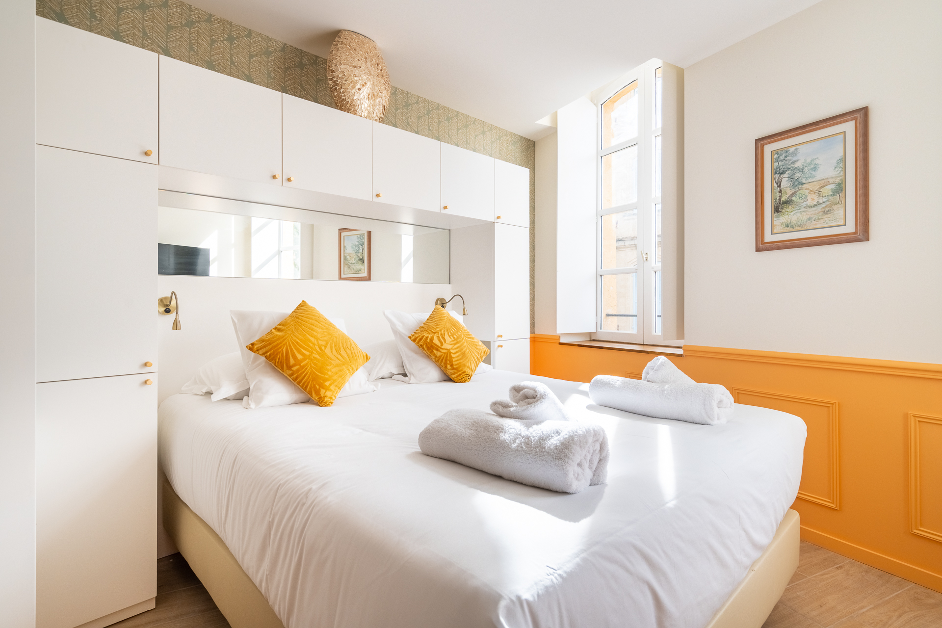 Chambre Deluxe : lit aux coussins moutarde et fenêtre cintrée