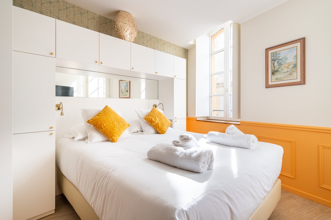 Chambre Deluxe : lit aux coussins moutarde et fenêtre cintrée
